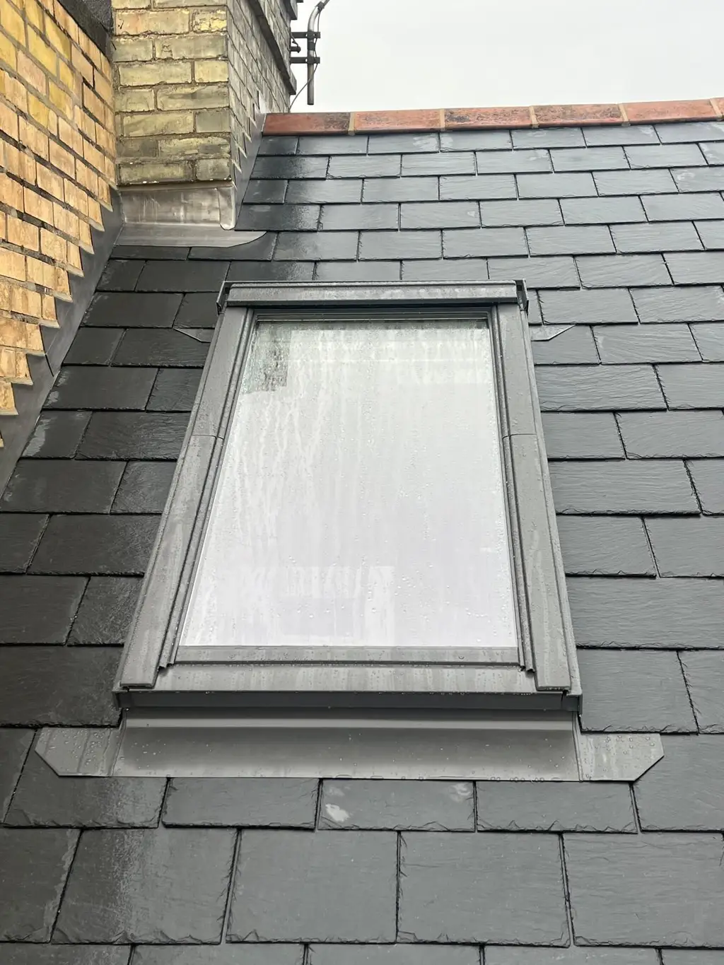Roof window with grey flashing in a slate roof by Carl Dunn Building & Roofing, Cambridge